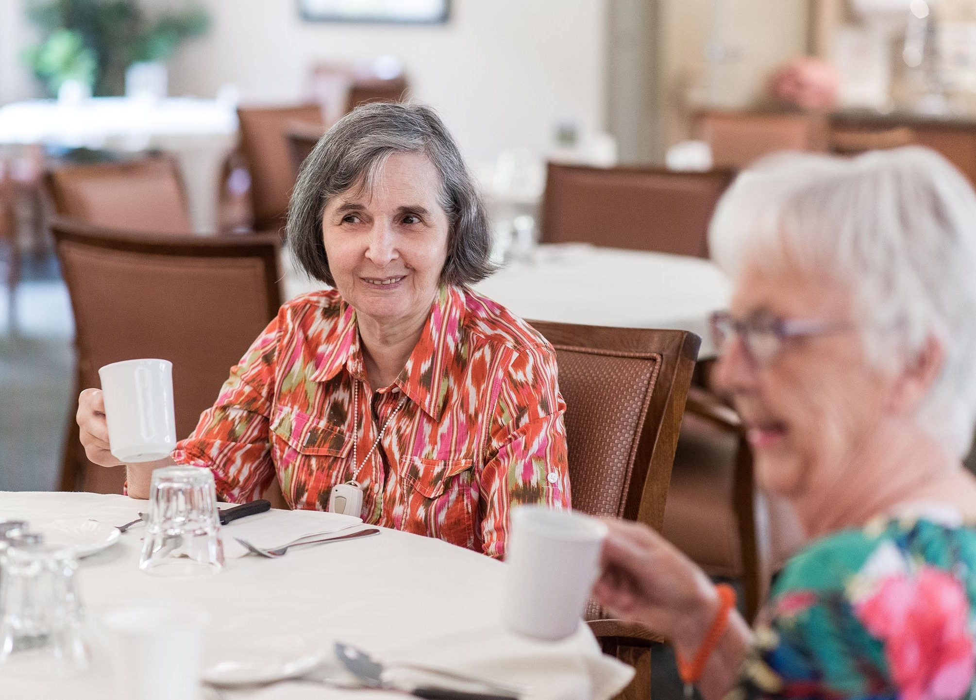 Two senior ladies enjoy coffee in dining room